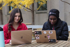 Two students working on their laptops at an outdoor table